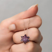 Purple star-shaped pendant on a gold chain held by a hand against a gray background