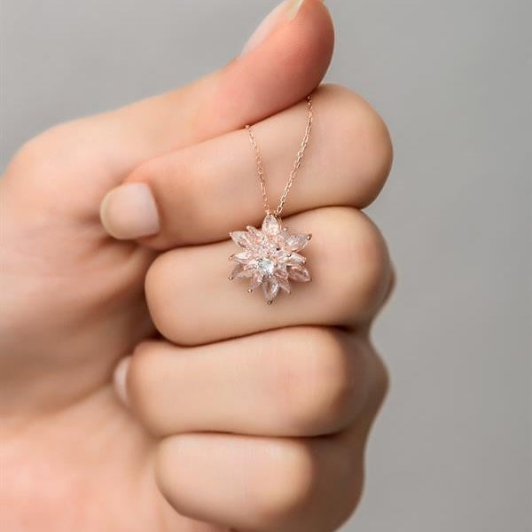 Hand holding a delicate pink flower-shaped necklace against a neutral background