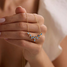 Gold necklace with blue stones held by a hand against a neutral background