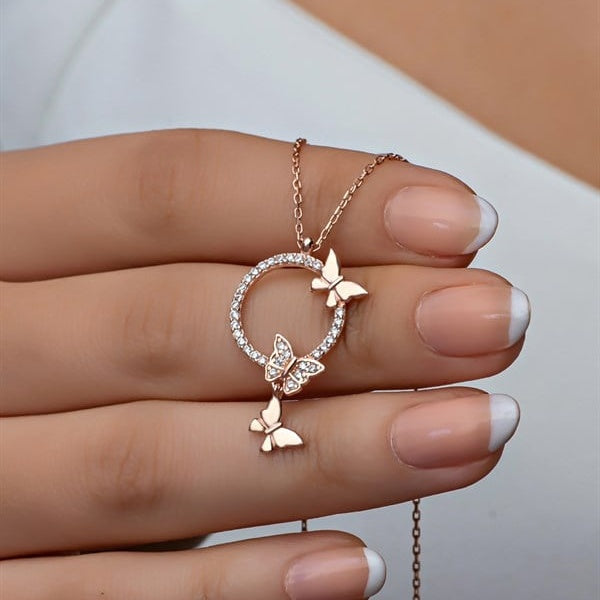 Rose gold butterfly necklace held by a hand with light nail polish.