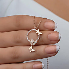 Rose gold butterfly necklace held by a hand with light nail polish.