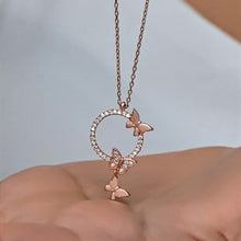 Rose gold necklace with butterfly pendant held by a hand against a light background