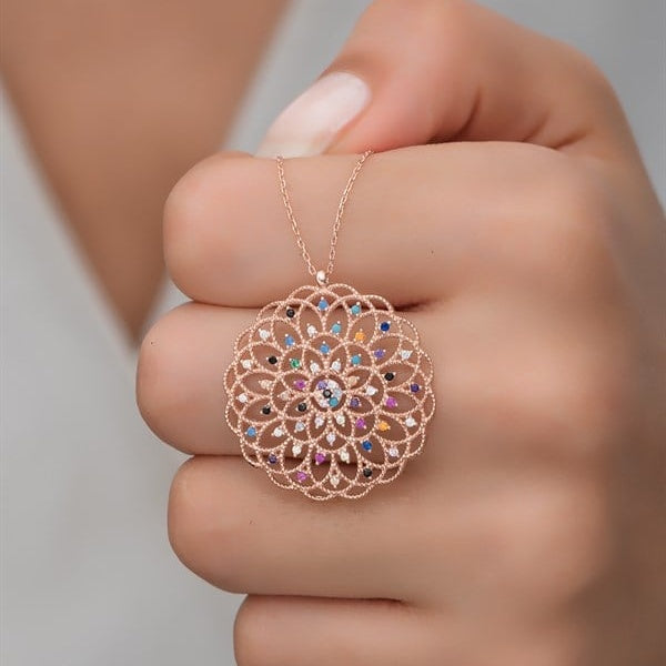 Decorative necklace with multicolored stones held between fingers against a neutral background