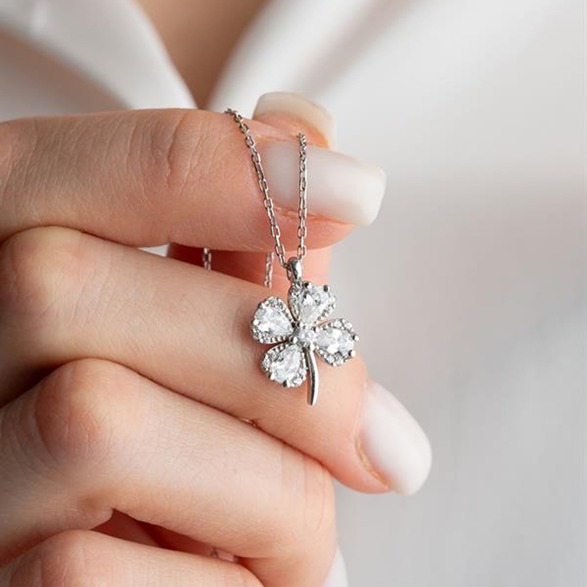 Silver four-leaf clover pendant held by a hand against a neutral background