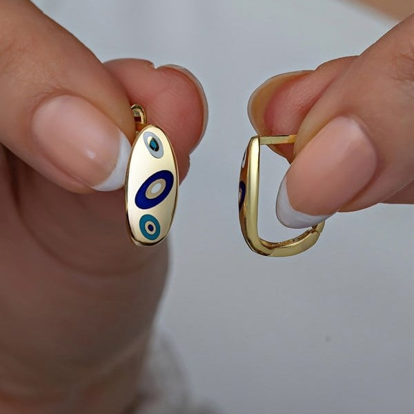 Gold earrings with blue and white designs held between fingers against a neutral background