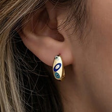 Close-up of an ear wearing a gold earring with blue and green accents.