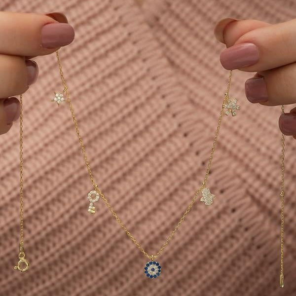 Gold necklace with various pendants held by hands against a textured pink background