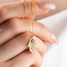 Gold necklace with a hamsa hand pendant held by a hand against a white background