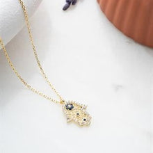 Gold necklace with a hamsa hand pendant on a white surface