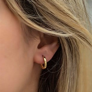 Close-up of a person wearing a gold hoop earring with blonde hair.