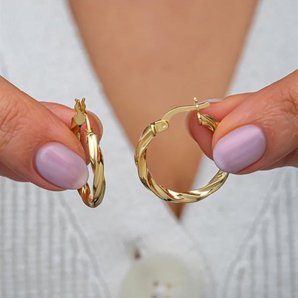 Gold hoop earrings held by a person with light purple nail polish on a blurred background
