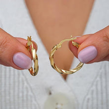 Gold hoop earrings held by a person with light purple nail polish on a blurred background