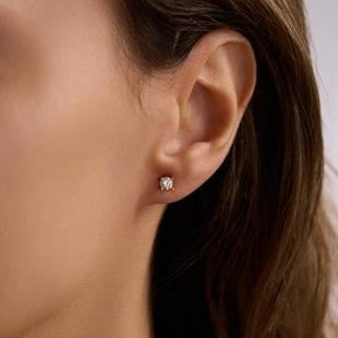 Close-up of an ear wearing a diamond stud earring with a blurred background