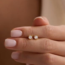 Gold stud earrings on a hand with a neutral background