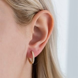 Close-up of an ear wearing a gold hoop earring with a blurred background