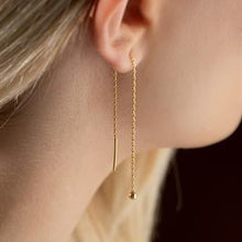 Gold earrings hanging from an ear with a blurred background