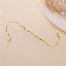 Gold bracelet on a beige surface with a shell in the background