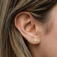 Close-up of an ear wearing a gold flower-shaped earring with hair partially covering the frame.