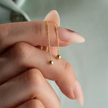 Gold necklace with small round pendants held by a hand against a neutral background