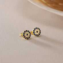 Gold earrings with blue gemstones on a beige surface
