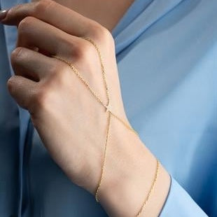 Close-up of a hand wearing a delicate gold bracelet against a light blue background