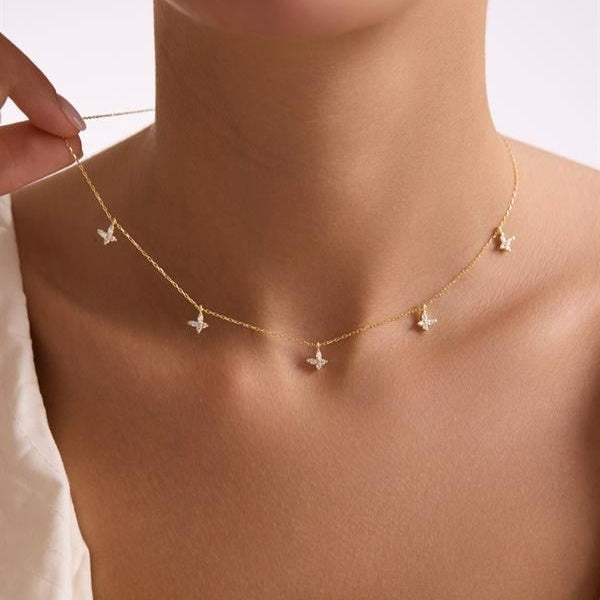 Gold necklace with butterfly pendants on a person's neck against a neutral background