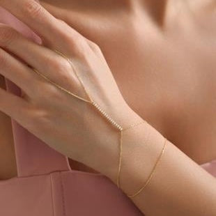 Close-up of a hand wearing a delicate gold bracelet against a soft pink background