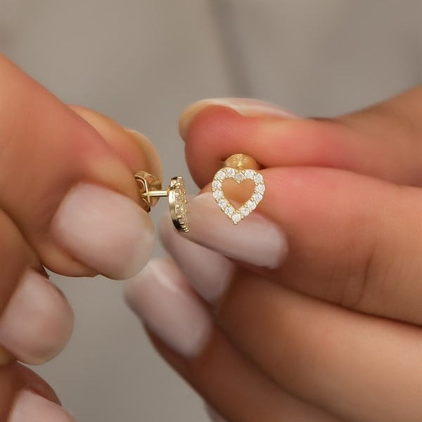 Heart-shaped diamond earrings held between fingers against a neutral background
