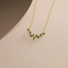Gold necklace with green gemstones on a beige surface