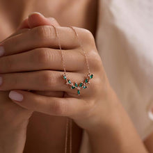 Rose gold necklace with green gemstones held by a hand against a neutral background