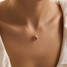 Gold necklace with a pink pendant on a person wearing a white top.