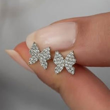 Butterfly-shaped earrings held between fingers against a neutral background