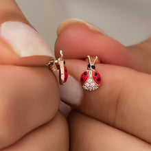 Red ladybug earrings with gold accents held between fingers against a neutral background