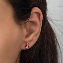 Close-up of an ear wearing a red earring with a small design.