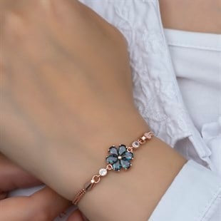 Rose gold bracelet with a blue gemstone on a wrist against a white background
