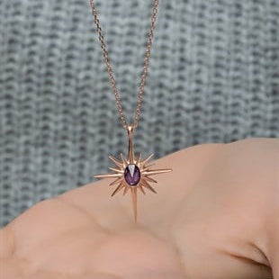 Rose gold necklace with a purple gemstone held by a hand against a textured gray background