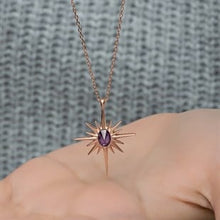 Rose gold necklace with a purple gemstone held by a hand against a textured gray background