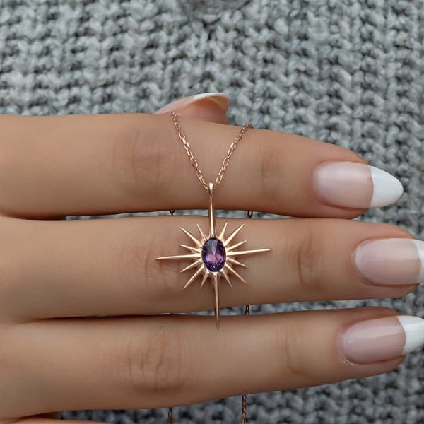 Gold necklace with a purple gemstone pendant on a hand against a textured gray background