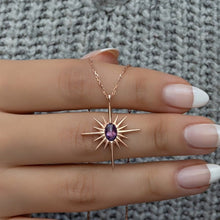Gold necklace with a purple gemstone pendant on a hand against a textured gray background