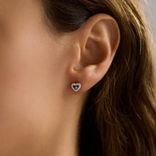 Close-up of an ear wearing a heart-shaped earring with a blue stone.