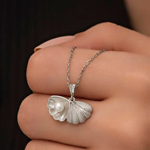 Silver necklace with a shell pendant featuring a pearl on a hand against a dark background