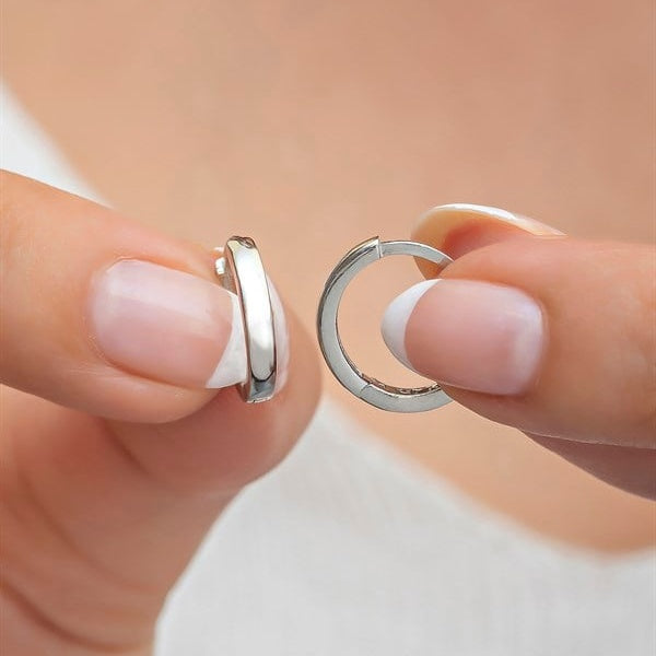 Two silver hoop earrings held between fingers against a neutral background