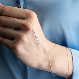 Close-up of a hand wearing a delicate silver bracelet against a light blue background