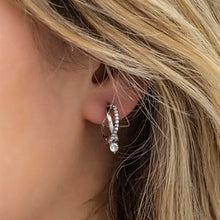Close-up of a person wearing a silver earring with a clear gemstone.