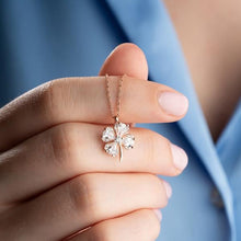 Four-leaf clover necklace held between fingers against a blue fabric background
