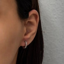 Close-up of an ear wearing a small hoop earring with a neutral background