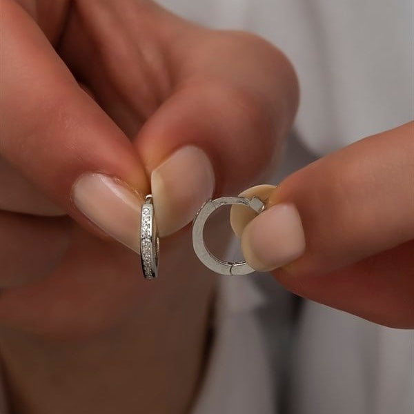 Close-up of hands holding two silver hoop earrings against a neutral background