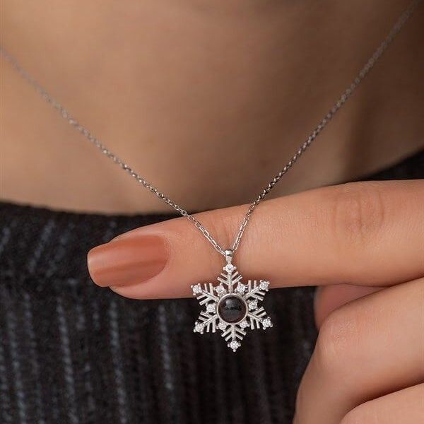 Silver snowflake pendant necklace held by a hand against a neutral background