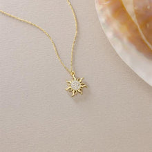 Gold sun-shaped necklace with clear stones on a beige surface
