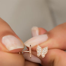 Rose gold butterfly earrings held between fingers with a neutral background